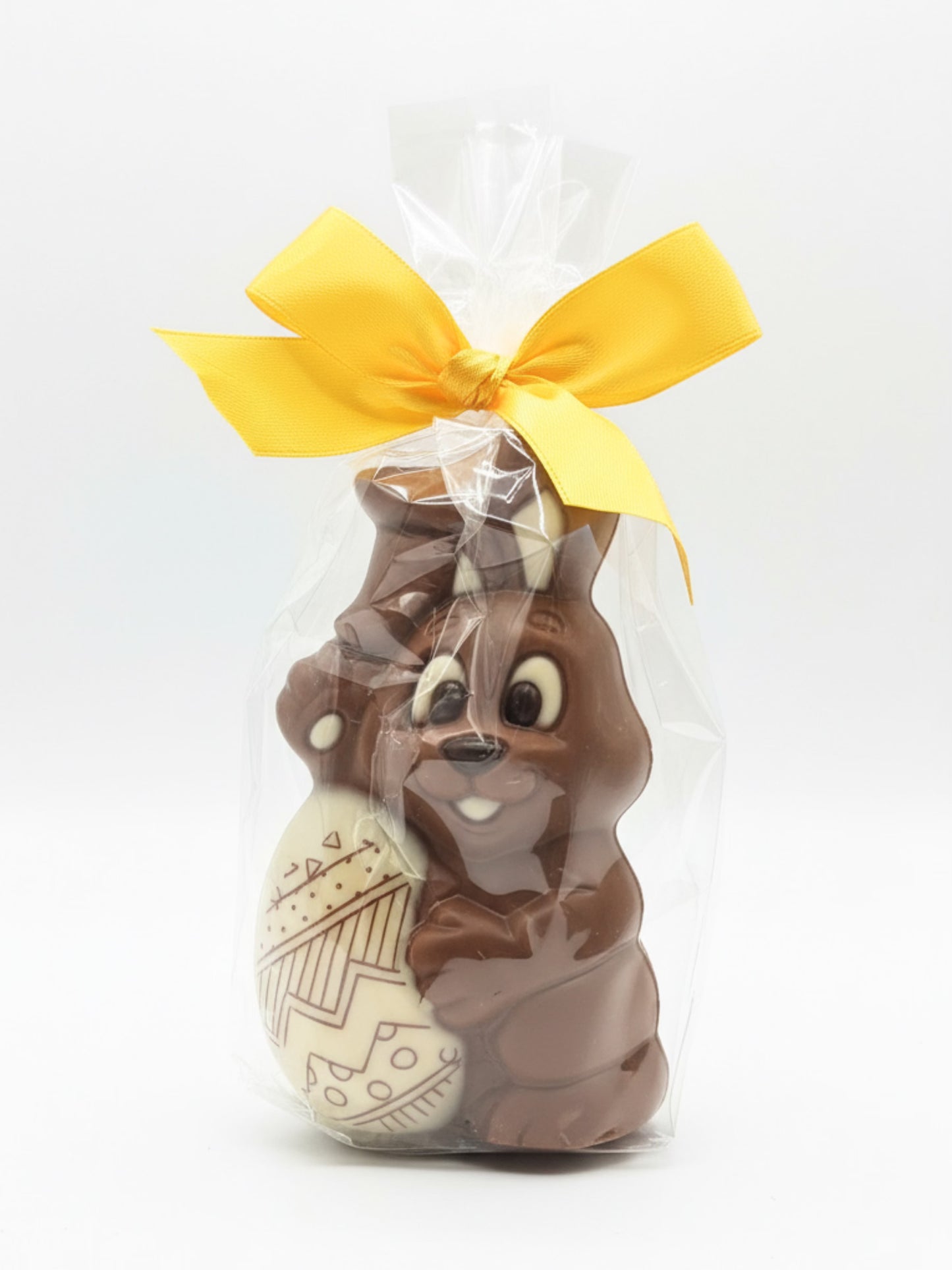 Schokoladen-Osterhase mit Dekor-Ei 75g von Sweet-Konzept, Osterhase aus Edelvollmilch-Schokolade mit verziertem Schokoladen-Ei in Folie mit gelber Schleife, erhältlich in der Dreyer Confiserie in der Rattenfängerstadt Hameln.